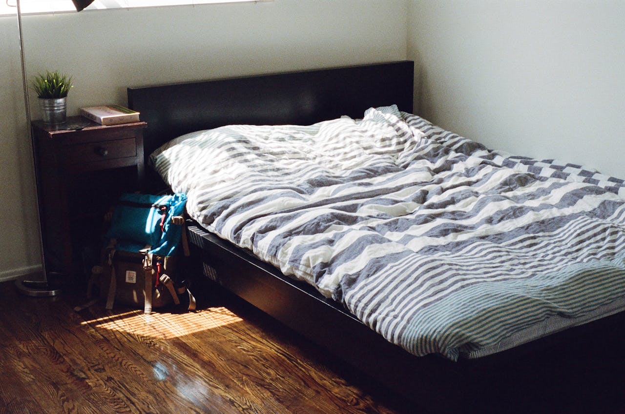 A minimalist bedroom featuring a striped bedding set and wooden furniture, enhanced by natural light.